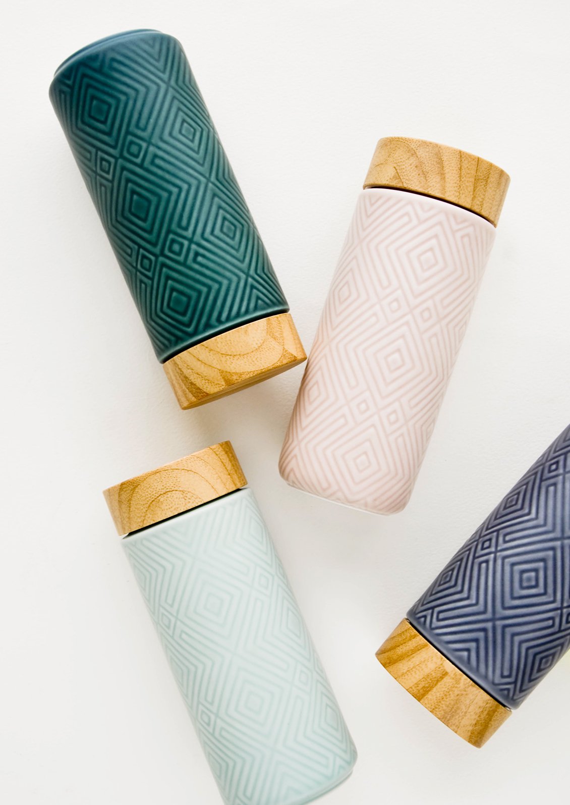 A scattered grouping of tall ceramic travel tumblers with tonal geometric patterns