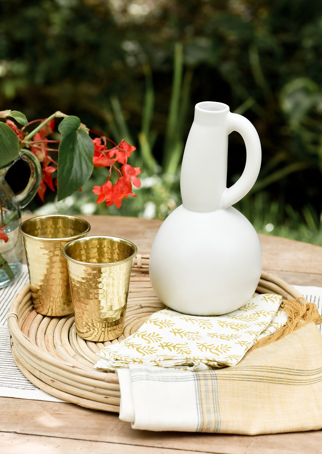 A table setting with ceramic pitcher and brass cups.
