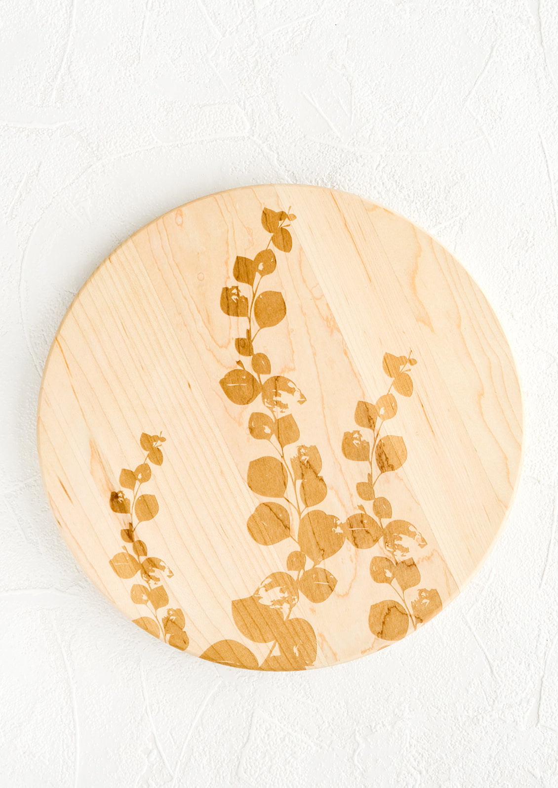 A round maple wood cutting board with laser etched eucalyptus print.