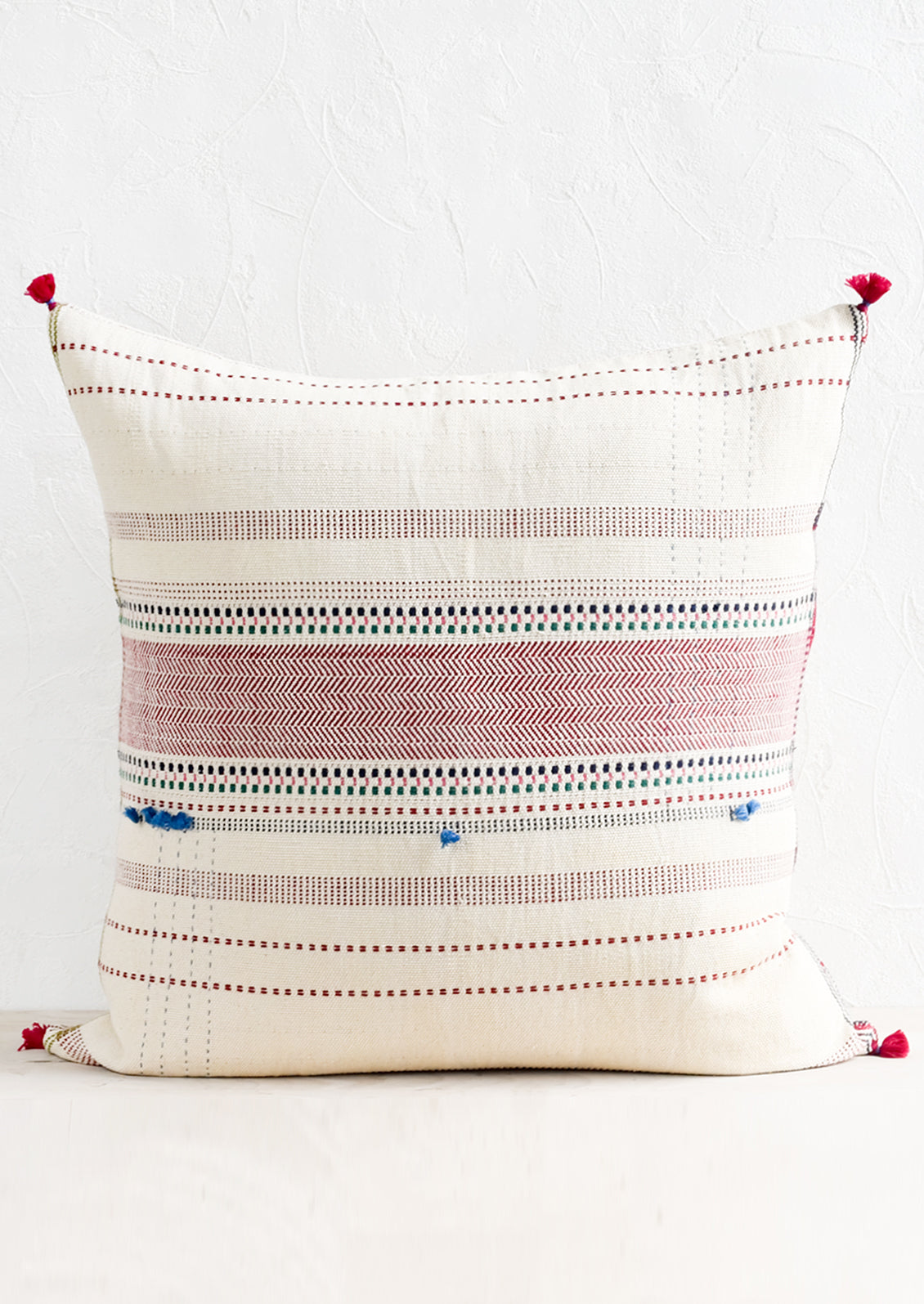 A cotton throw pillow with multicolor and red embroidery and tassel detailing.