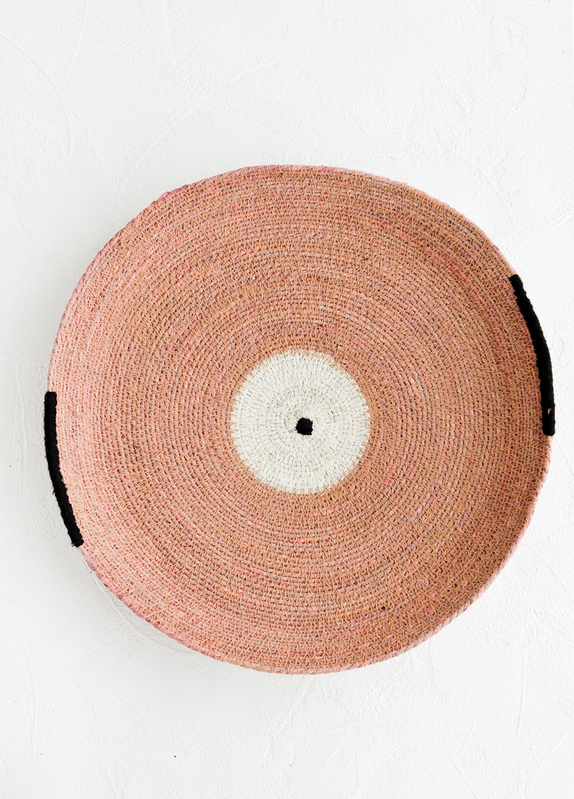 A round platter/tray made from woven seagrass in pink, white and black.