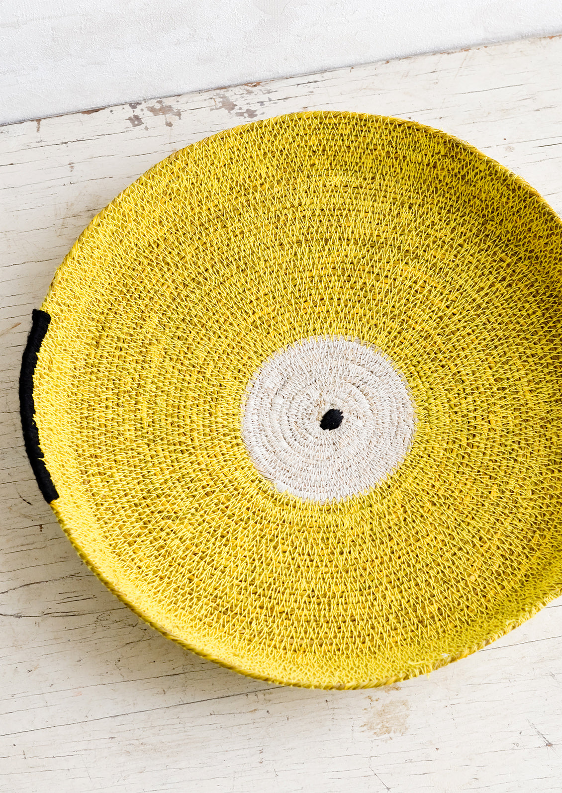 A round platter/tray made from woven seagrass in yellow, white and black.