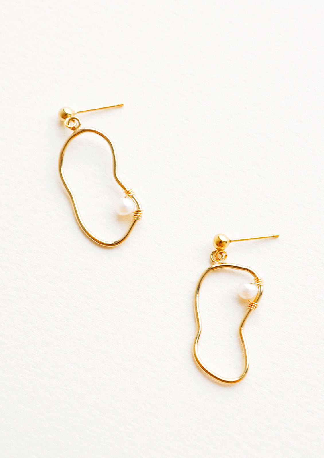 Dangling earrings featuring asymmetric round gold charm made from a slim gold hoop, with one pearl attached with wrapped wire.