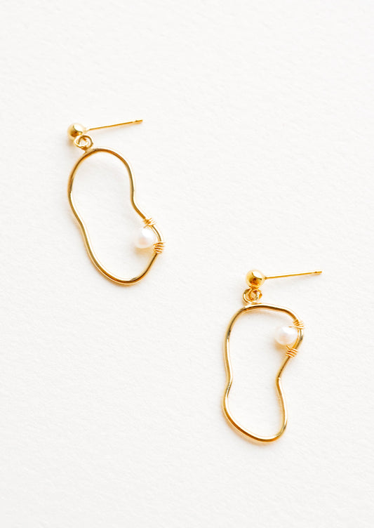 Dangling earrings featuring asymmetric round gold charm made from a slim gold hoop, with one pearl attached with wrapped wire.