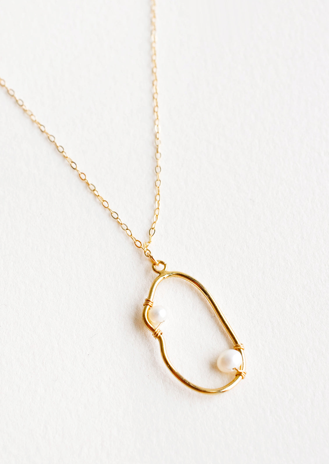 Gold necklace with asymmetric round gold charm made from a slim gold hoop, with two pearls attached with wrapped wire.