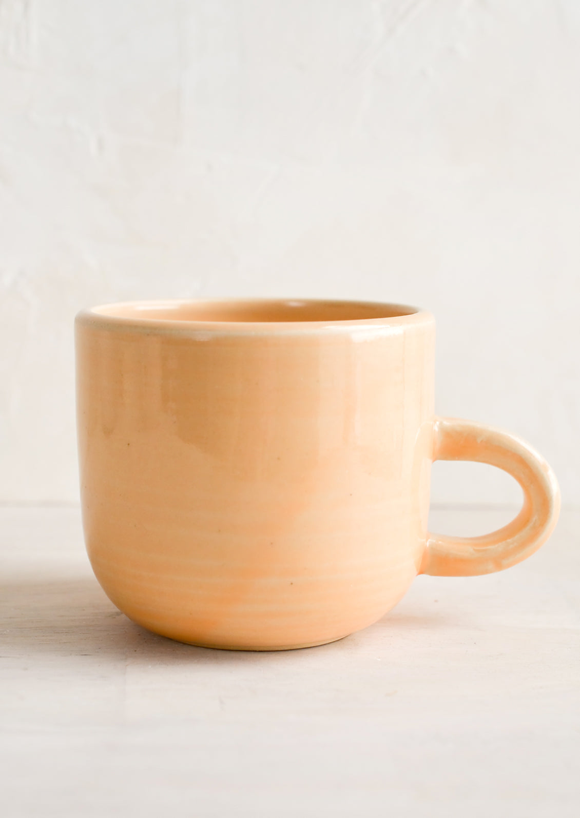 A short ceramic coffee mug in glossy pastel peach glaze.