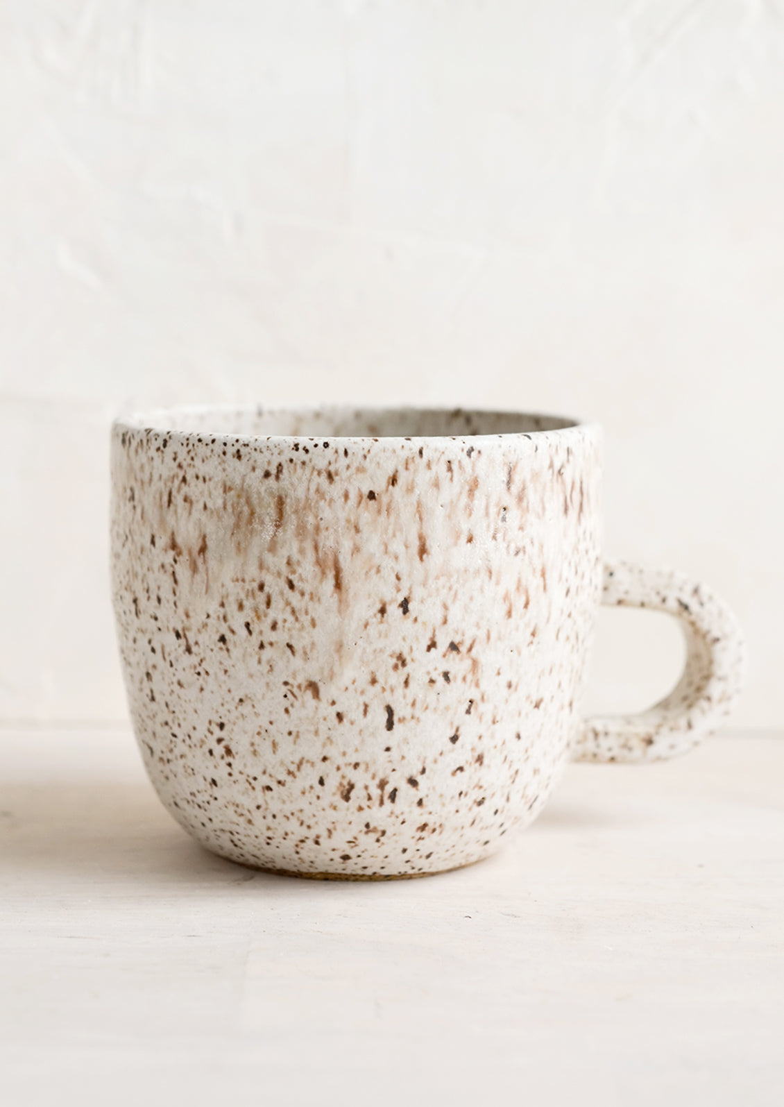 A short ceramic coffee mug in matte natural glaze with brown speckles.