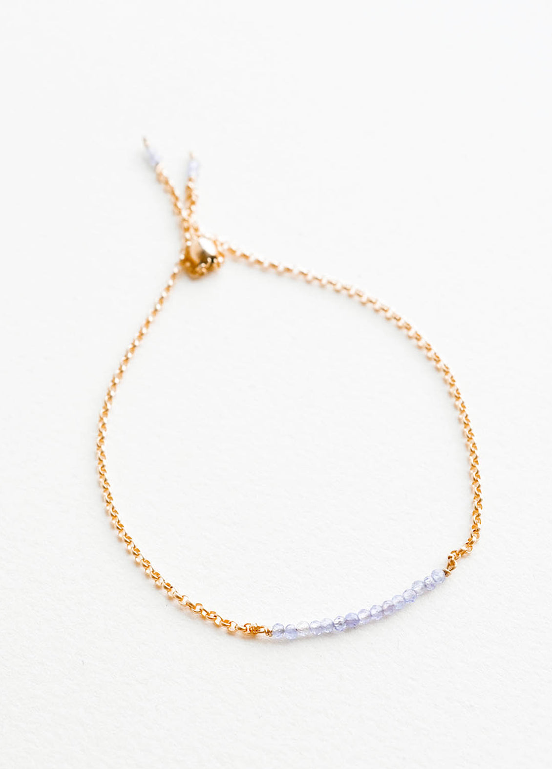 A delicate gold chain bracelet featuring a row of miniature light blue gemstones.