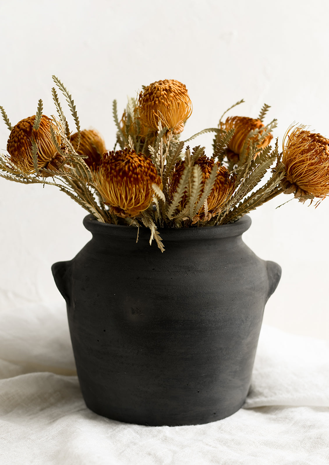 A black clay pot with dried mini proteas.