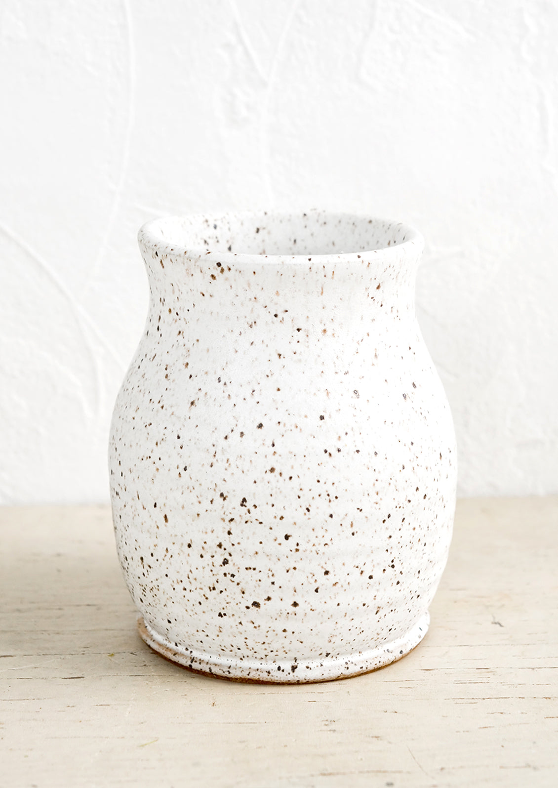 A curvy ceramic vase in matte white glaze with brown speckles.