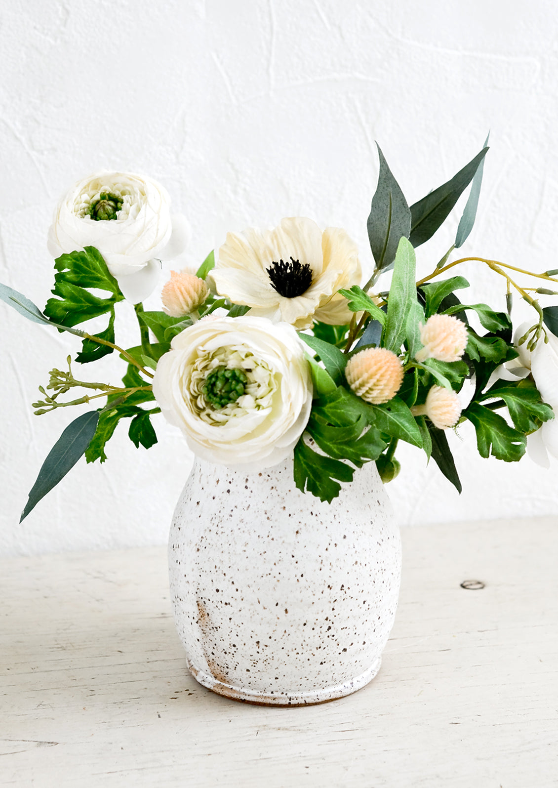 A speckled ceramic vase with a floral arrangement of white anemone and ranculus.