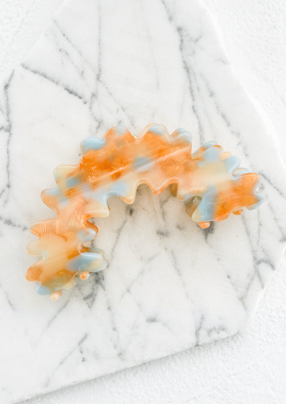 An orange and blue acetate hair claw in squiggly arch shape.