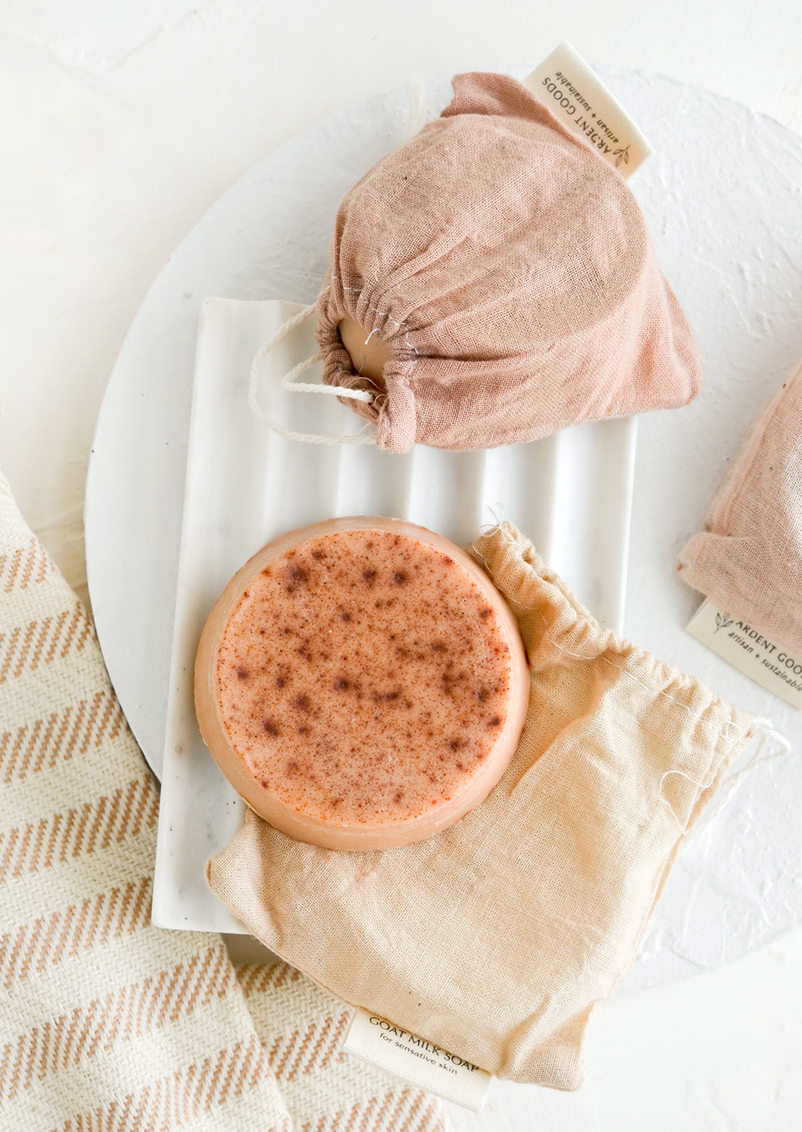 A round soap bar with naturally dyed muslin pouches on marble soap dish.