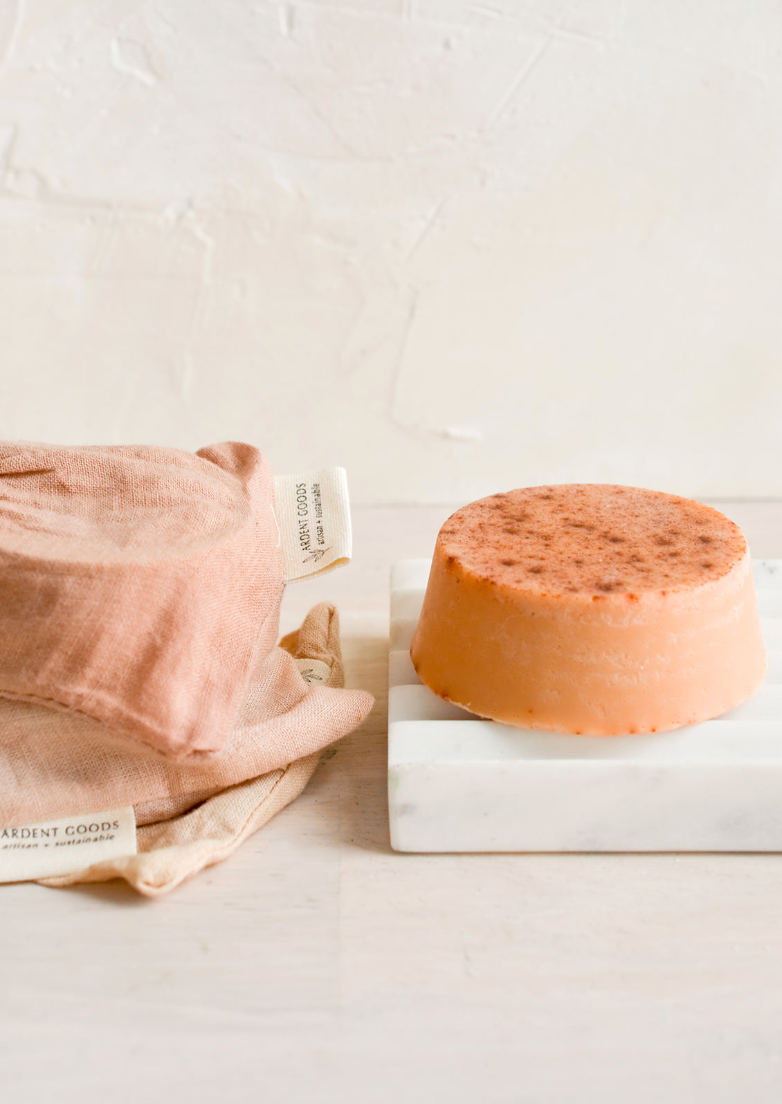 A round soap bar with naturally dyed muslin pouches on marble soap dish.