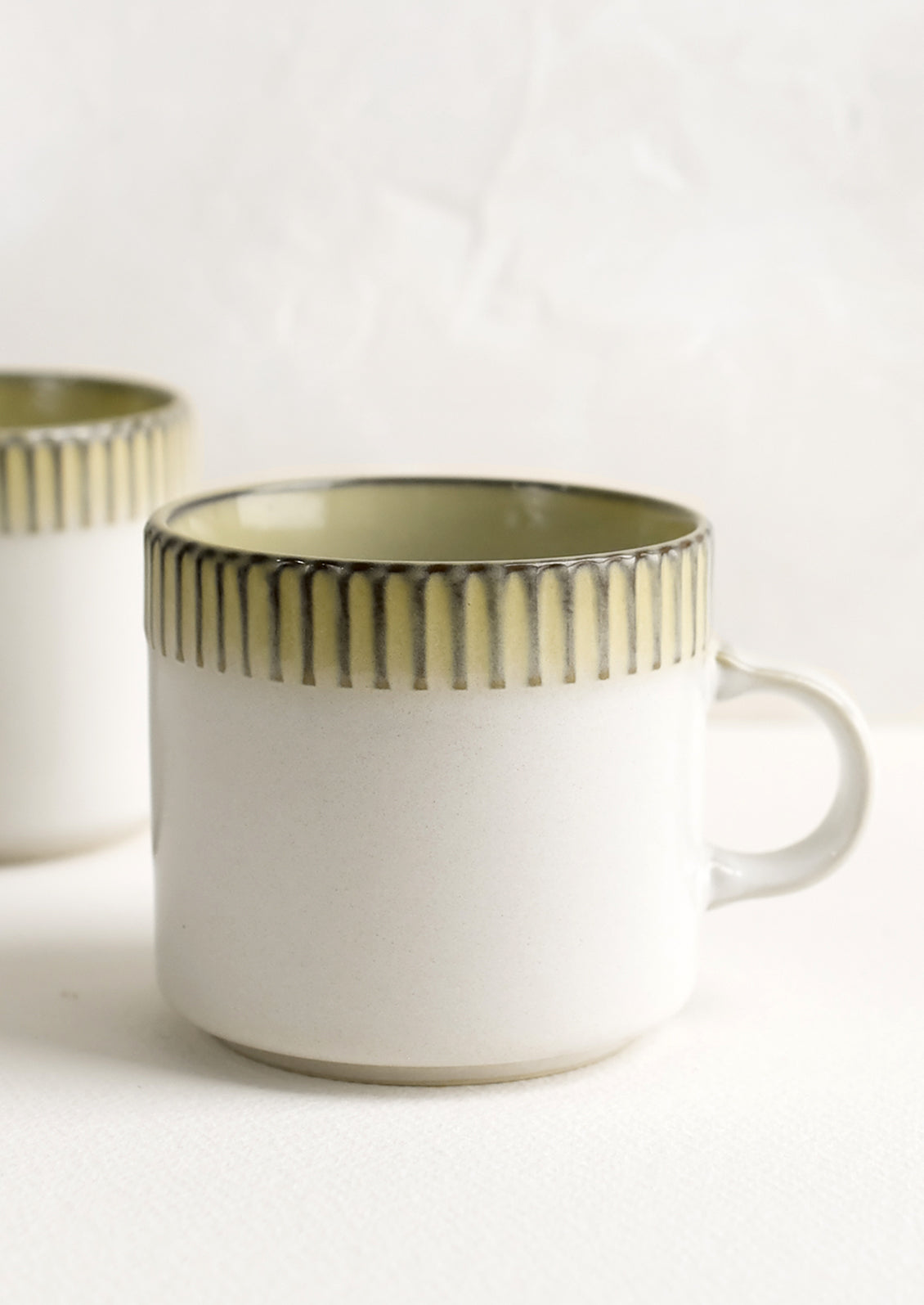 A ceramic mug in white with ribbed yellow border along rim.