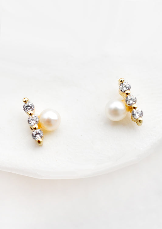 A pair of stud earrings with pearl aligned next to three crystal bar.