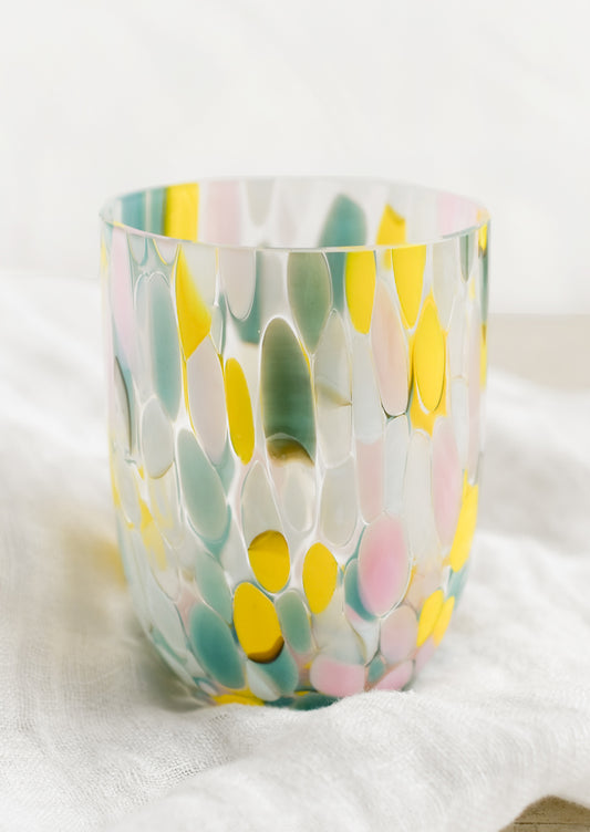 A handmade speckled glass juice cup with teal, yellow and pink spots.