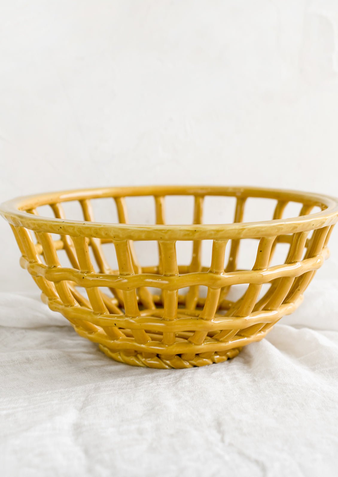 An open weave bowl made from mustard-colored ceramic.