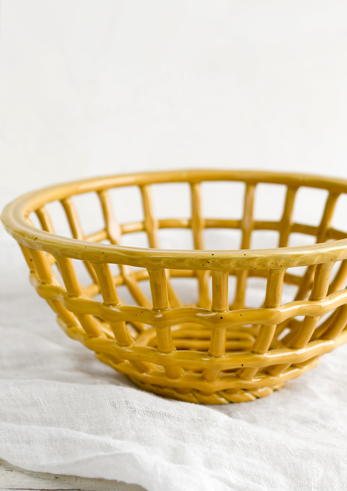 An open weave bowl made from mustard-colored ceramic.