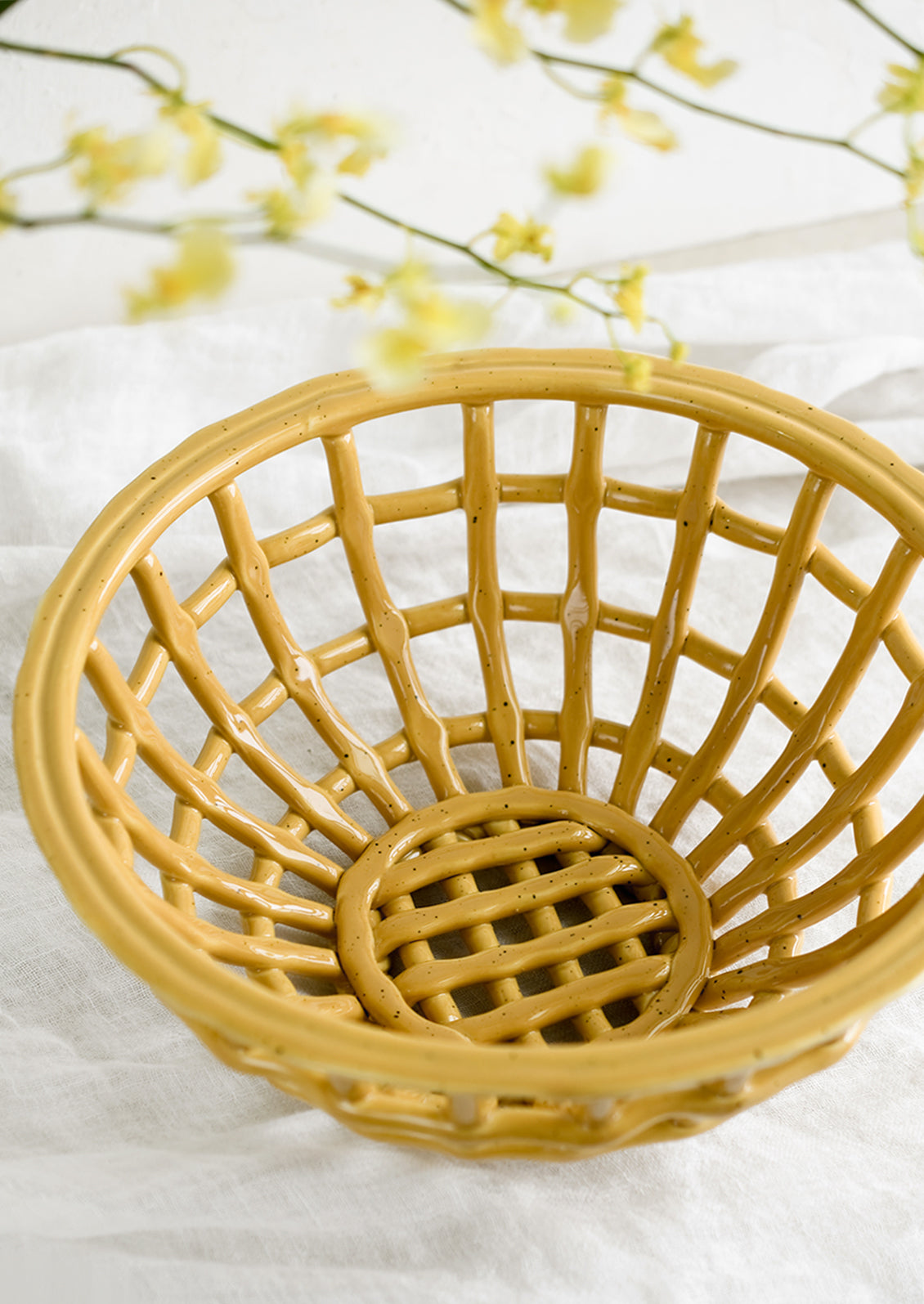 An open weave bowl made from mustard-colored ceramic.