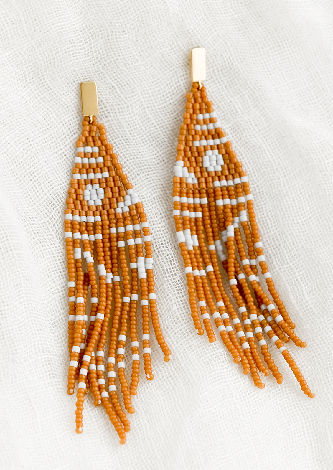 A pair of beaded earrings with geometric pattern in cedar and white.