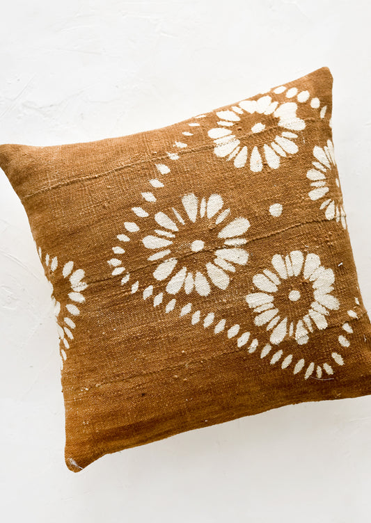 A brown mudcloth throw pillow with white floral motif.