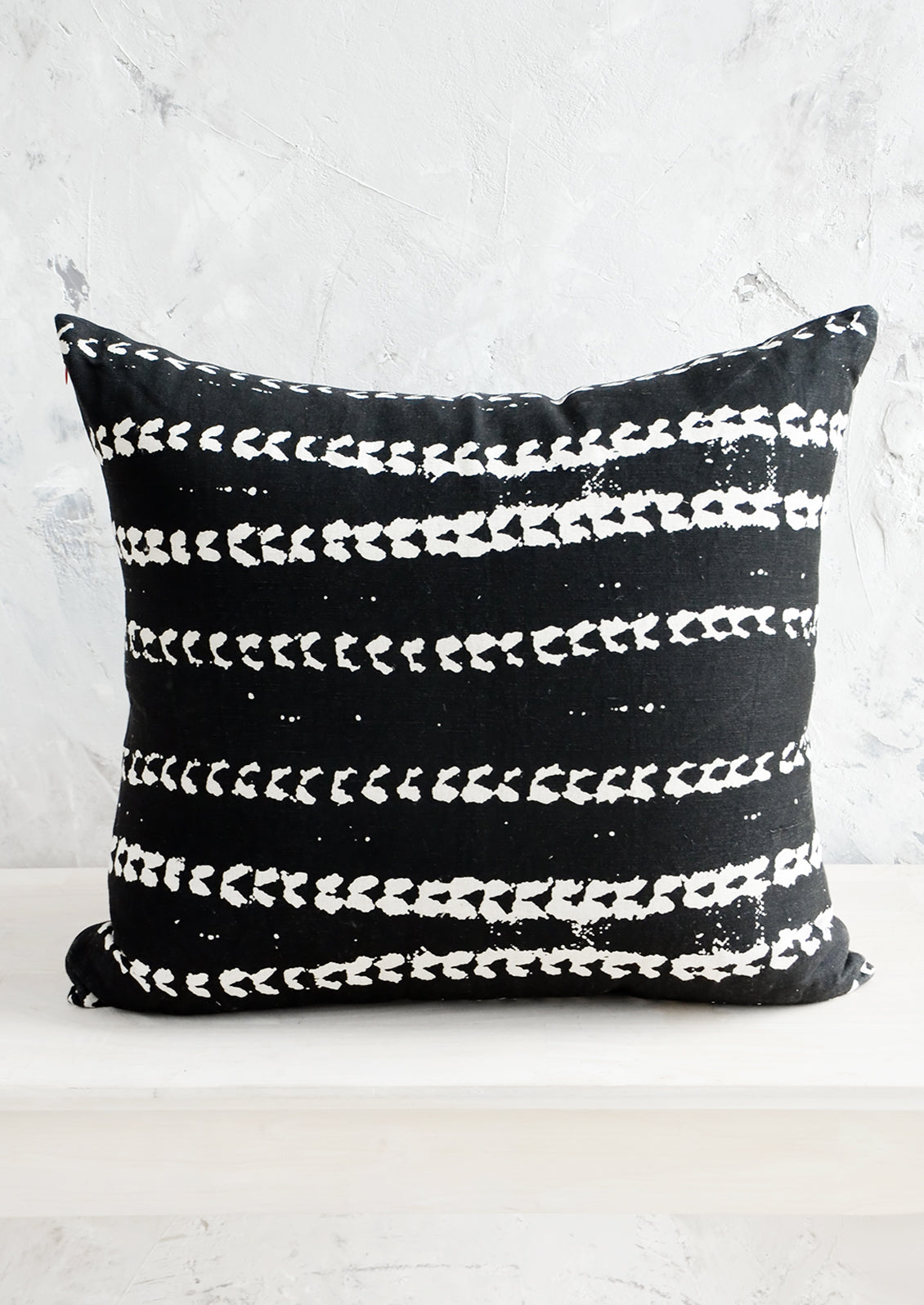 Square throw pillow in black linen with horizontal batik print stripe pattern in white.