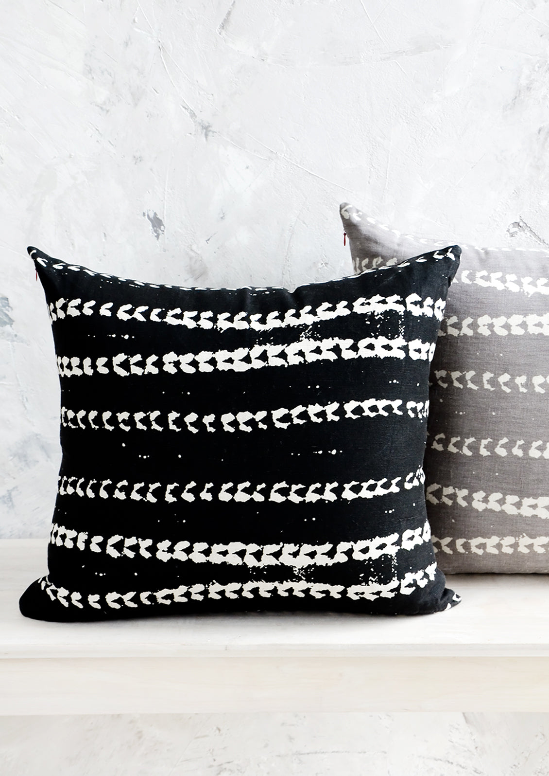 Two square throw pillows, one black and one grey, with white batik printed stripes.