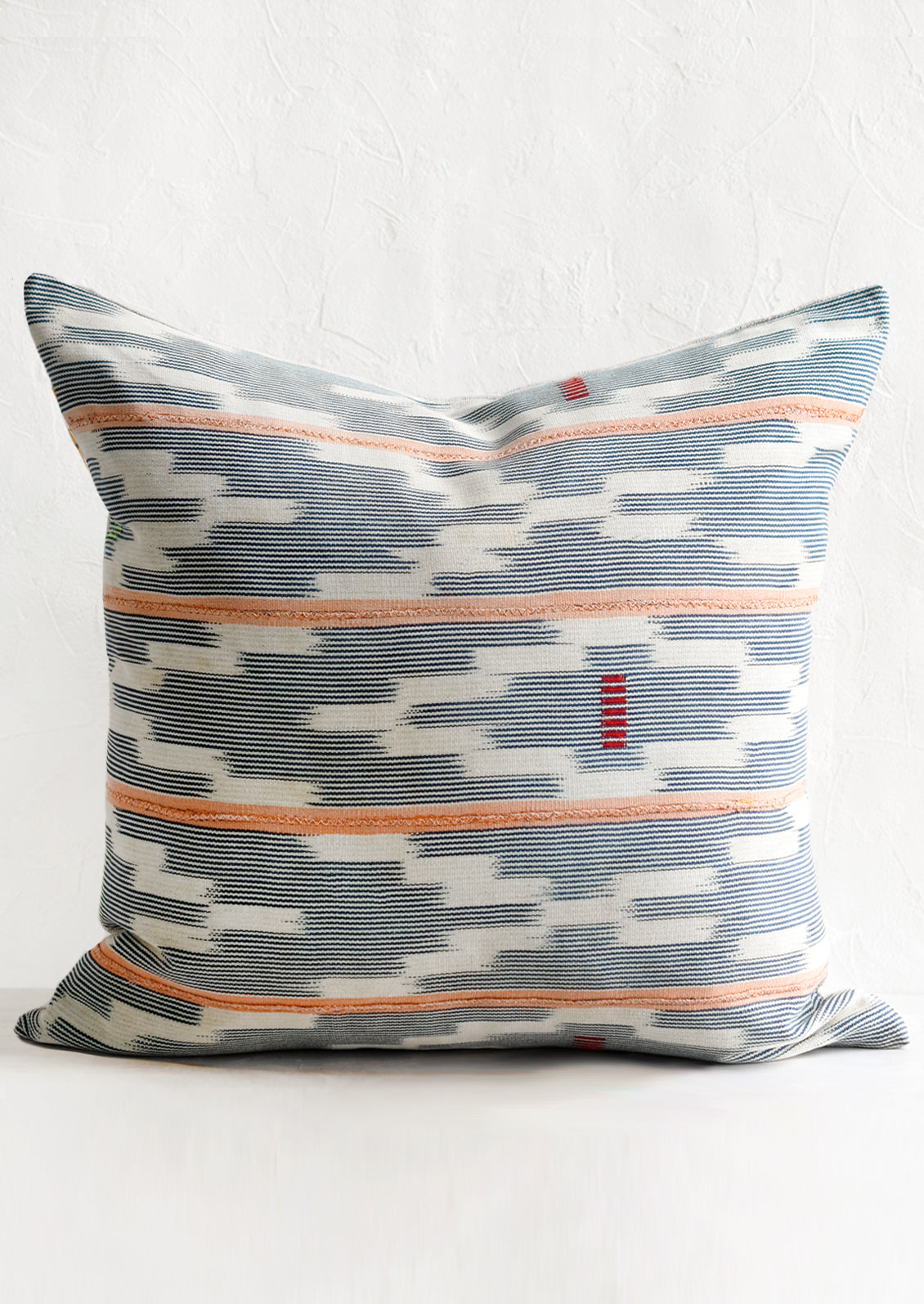 A throw pillow made from indigo baule fabric with peach stripes.