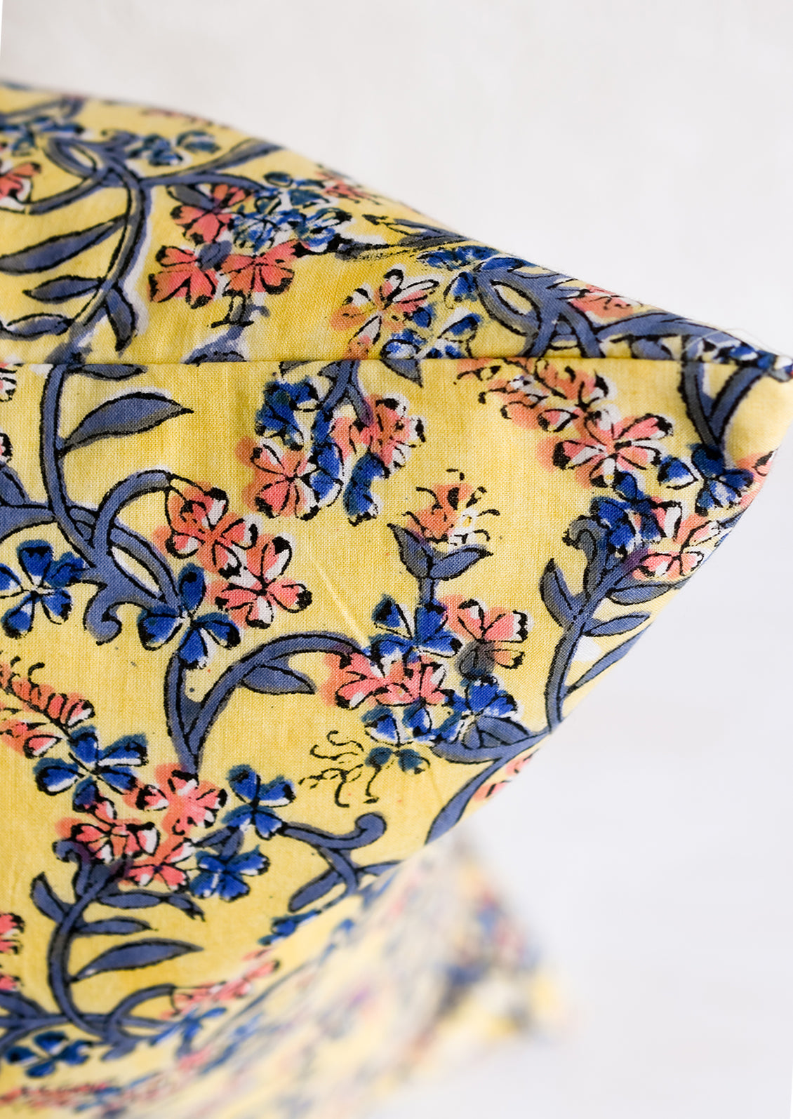 A block printed throw pillow in yellow with blue and pink floral print.