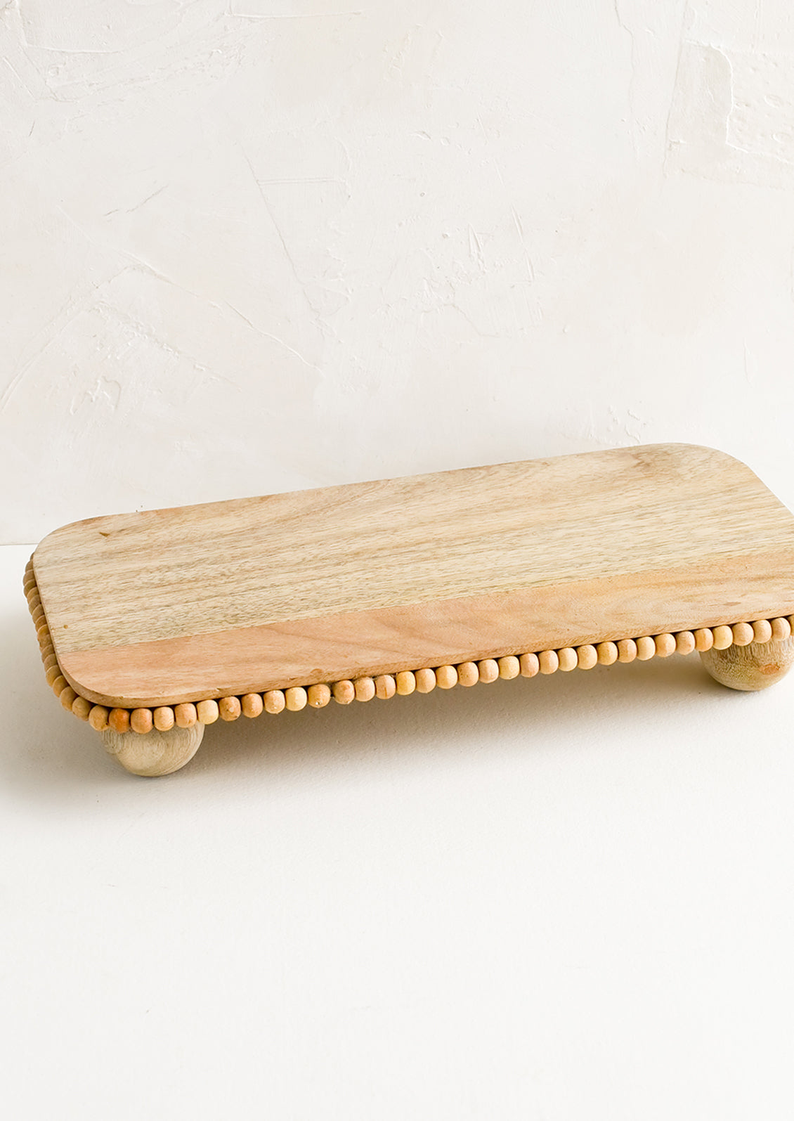 A rectangular wooden riser with round feet and beaded detail.