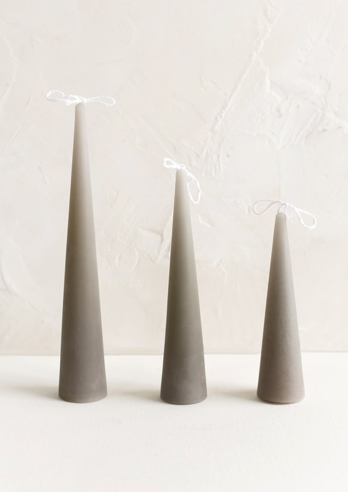 Three cone-shaped taper candles in light grey.