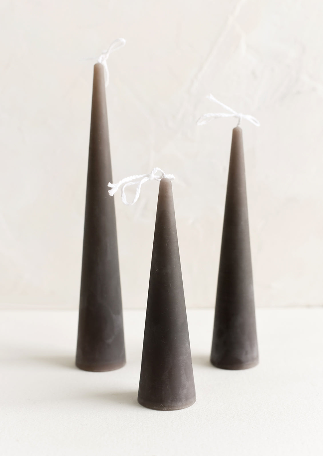 Three lit cone-shaped taper candles in dark grey.