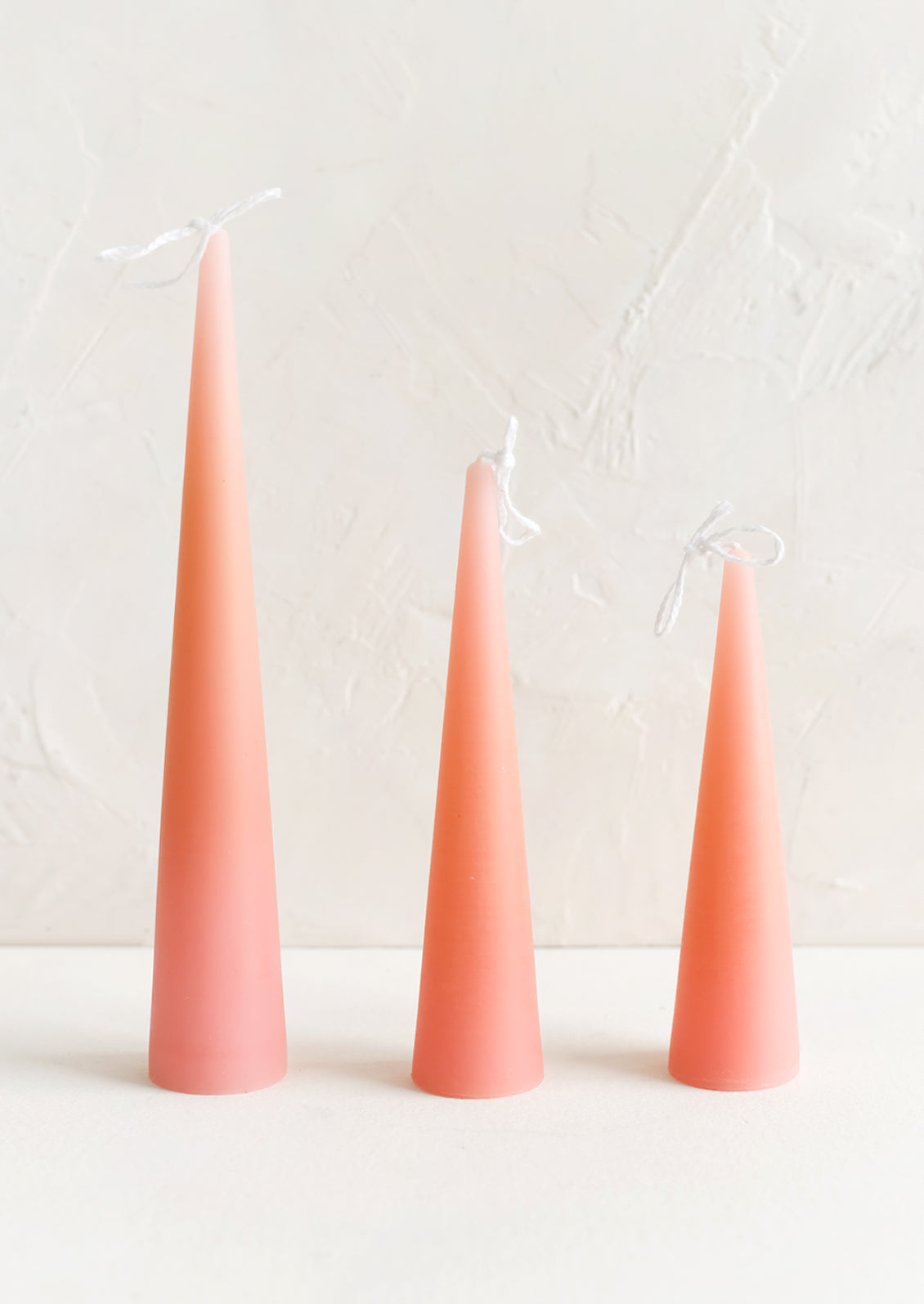 Three lit cone-shaped taper candles in pink peach.