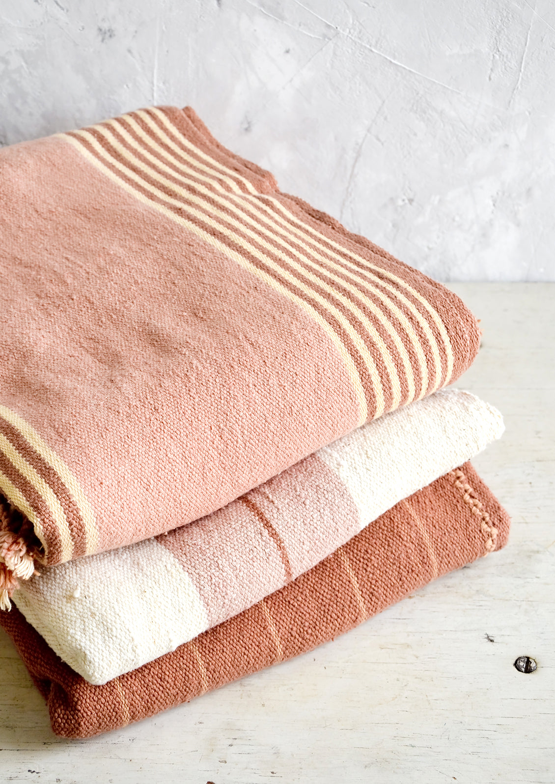 Stack of naturally colored cotton throws in pink, cream and terracotta