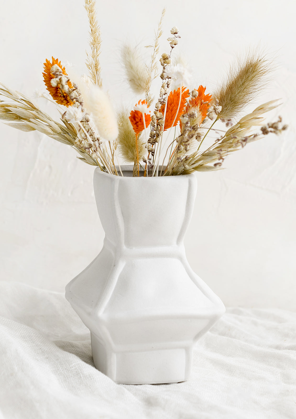 A short geometric vase in white ceramic, shown with dried flowers.