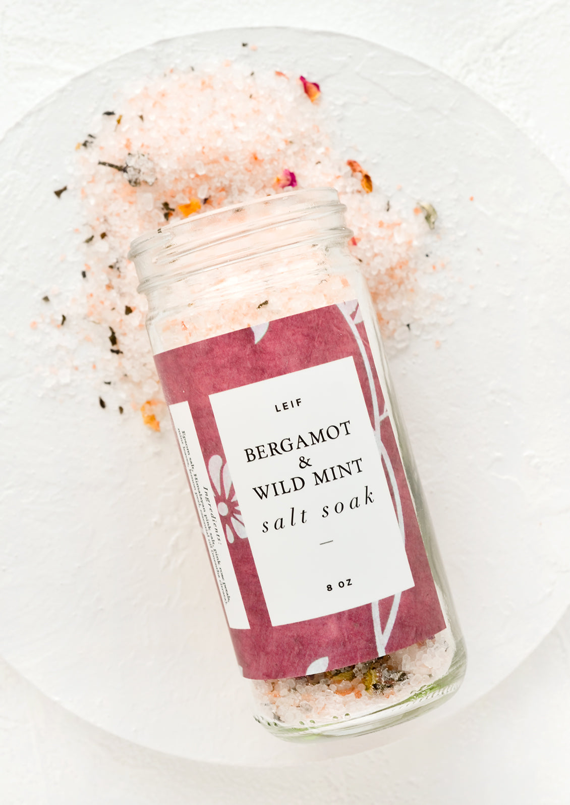 Bergamot and wild mint bath salt soak spilling out of a glass jar.