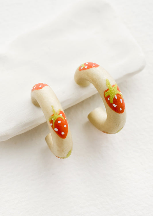 A pair of painted wood hoop earrings with strawberry pattern.