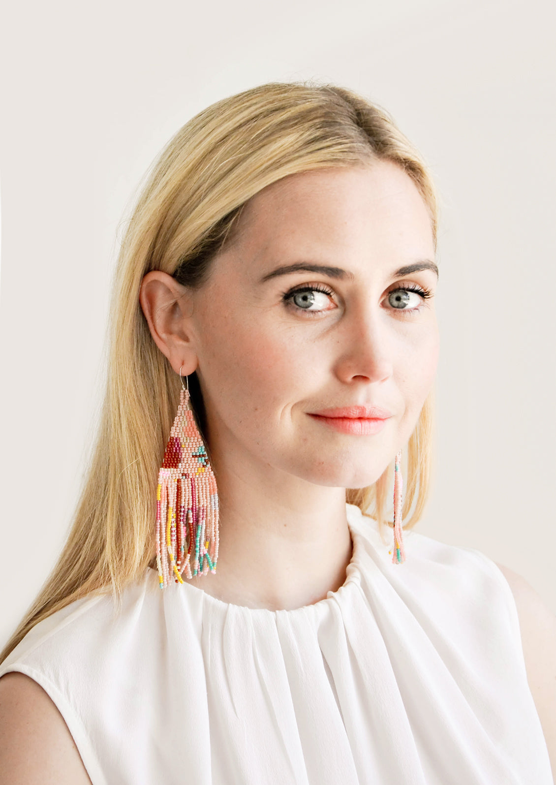 Model wears multicolored fringe beaded earrings and white blouse.