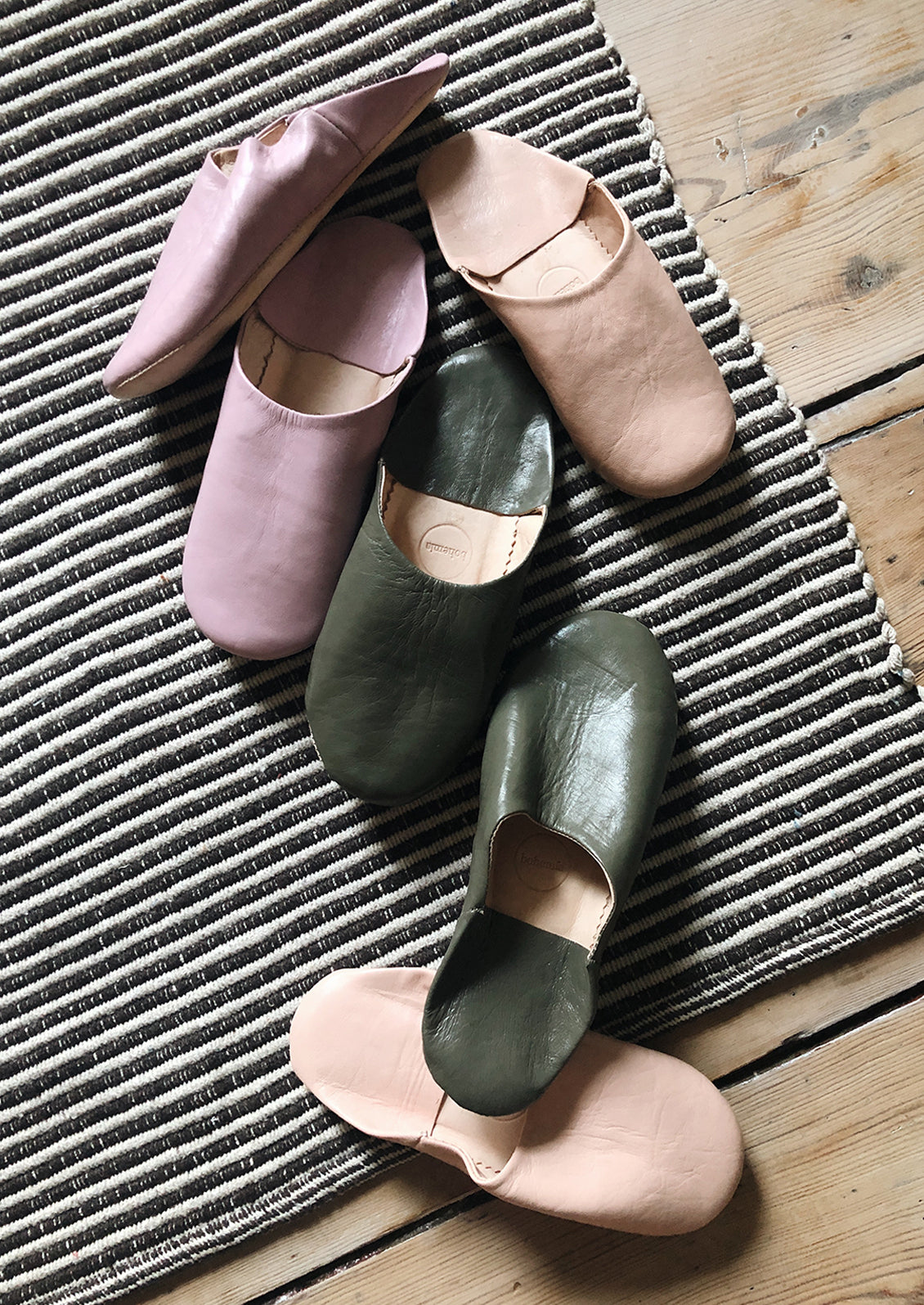 Different colors of leather house slippers scattered across a striped rug.