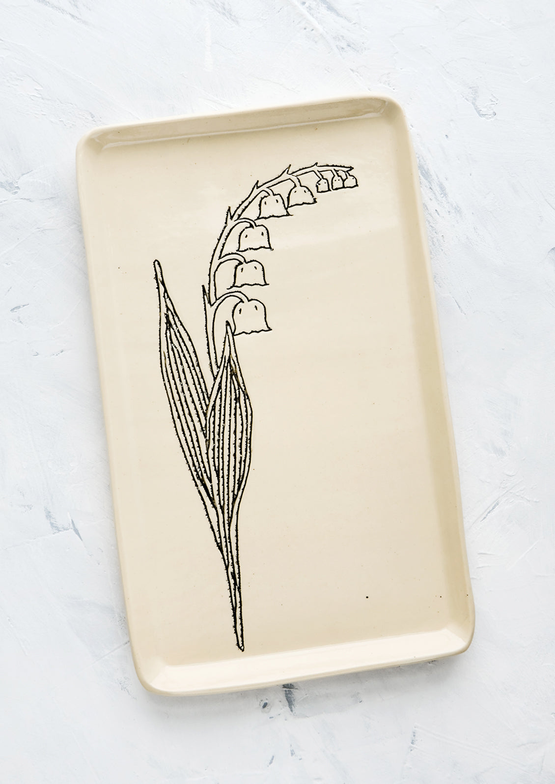 A rectangular ceramic tray in natural bisque color with an etched black drawing of Lily Of the Valley flower.