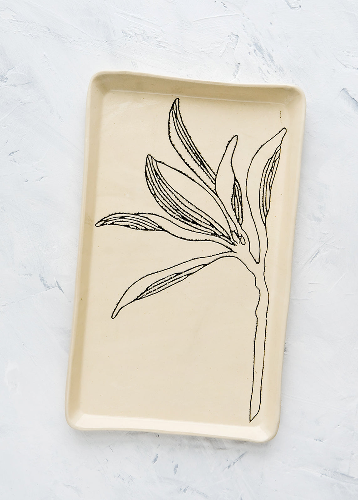 A rectangular ceramic tray in natural bisque color with an etched black drawing of a Magnolia branch.