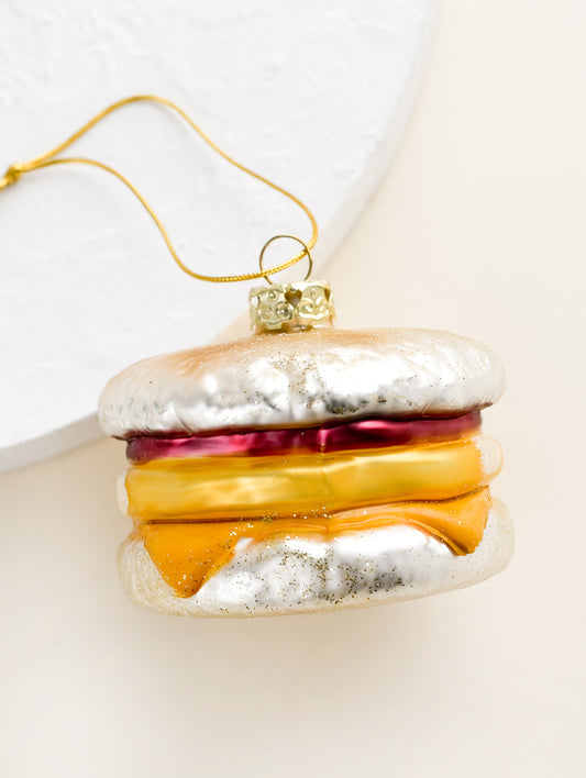 A decorative glass ornament in the shape of an egg breakfast sandwich on english muffin.