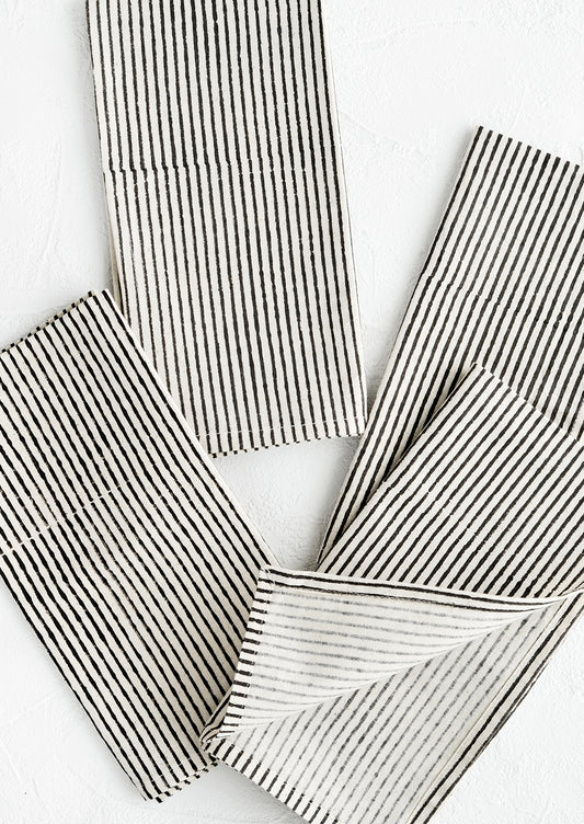 Scattered folded fabric napkins in natural cotton with hand-drawn line pattern in black.