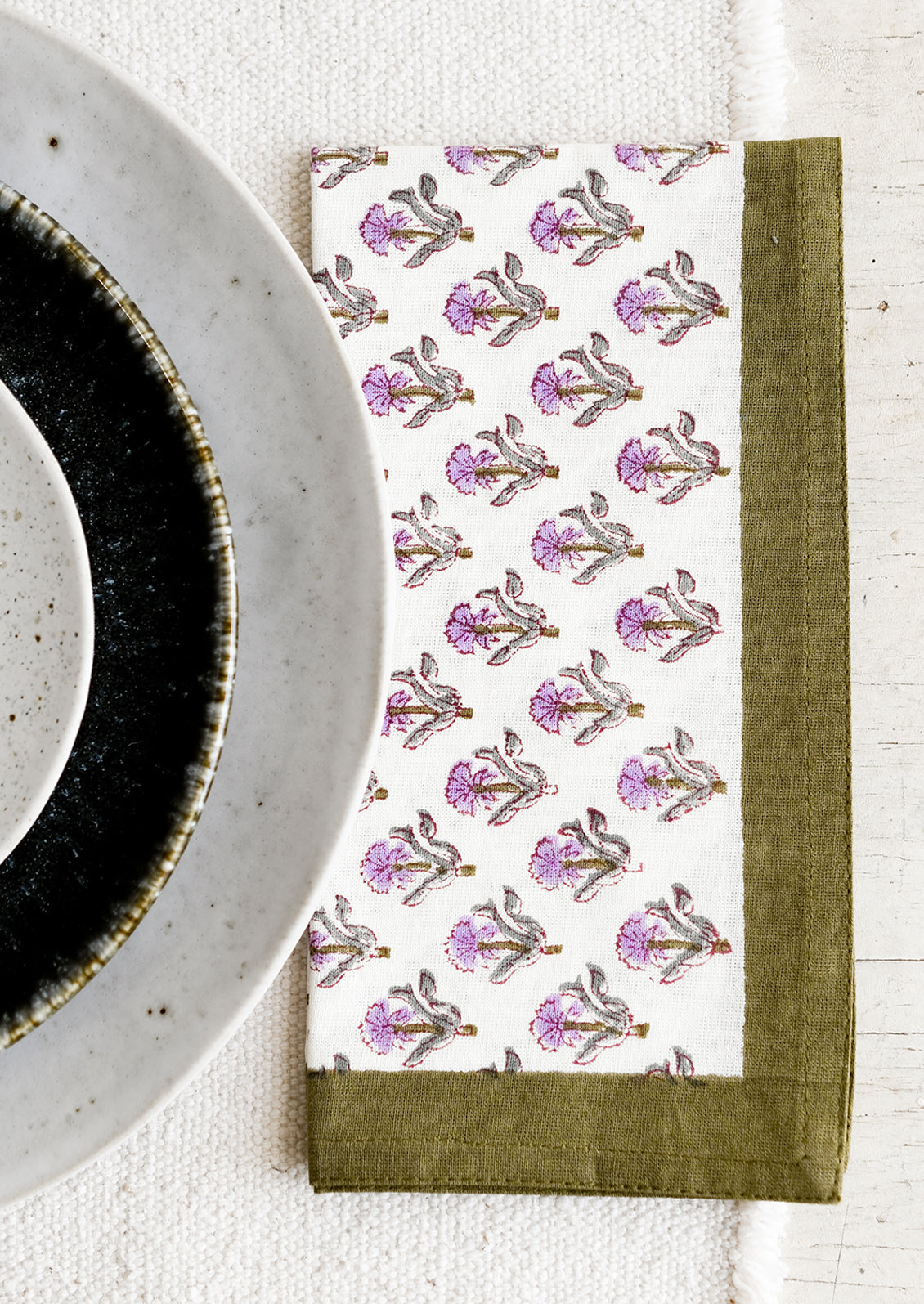 A pair of block printed floral napkins in olive and purple.