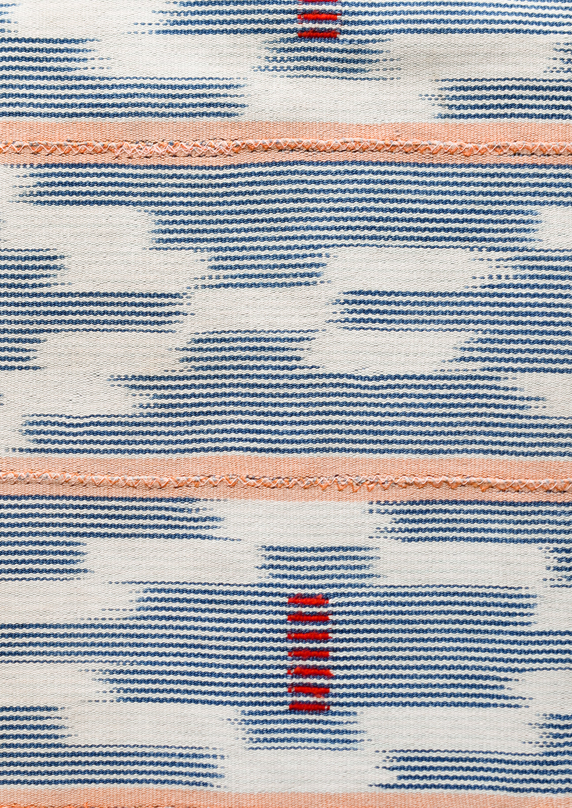 A throw pillow made from indigo baule fabric with peach stripes.