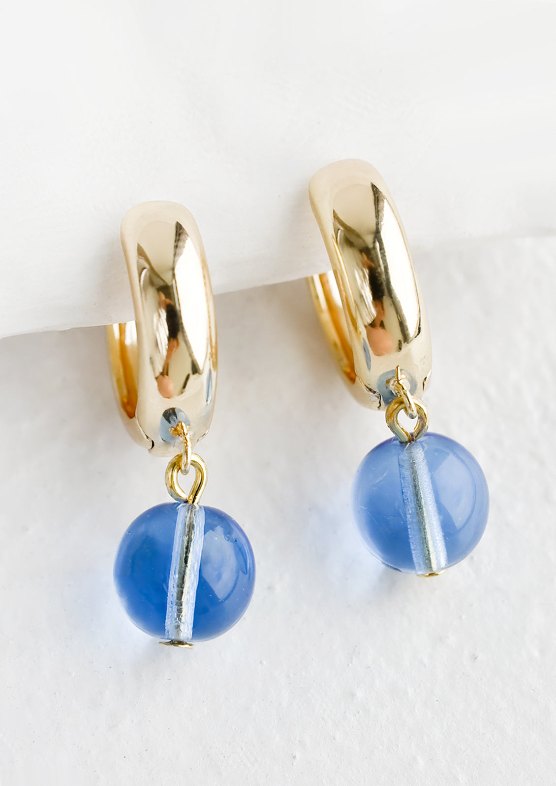 A pair of gold huggie hoop earrings with single spherical blue glass bead detail.