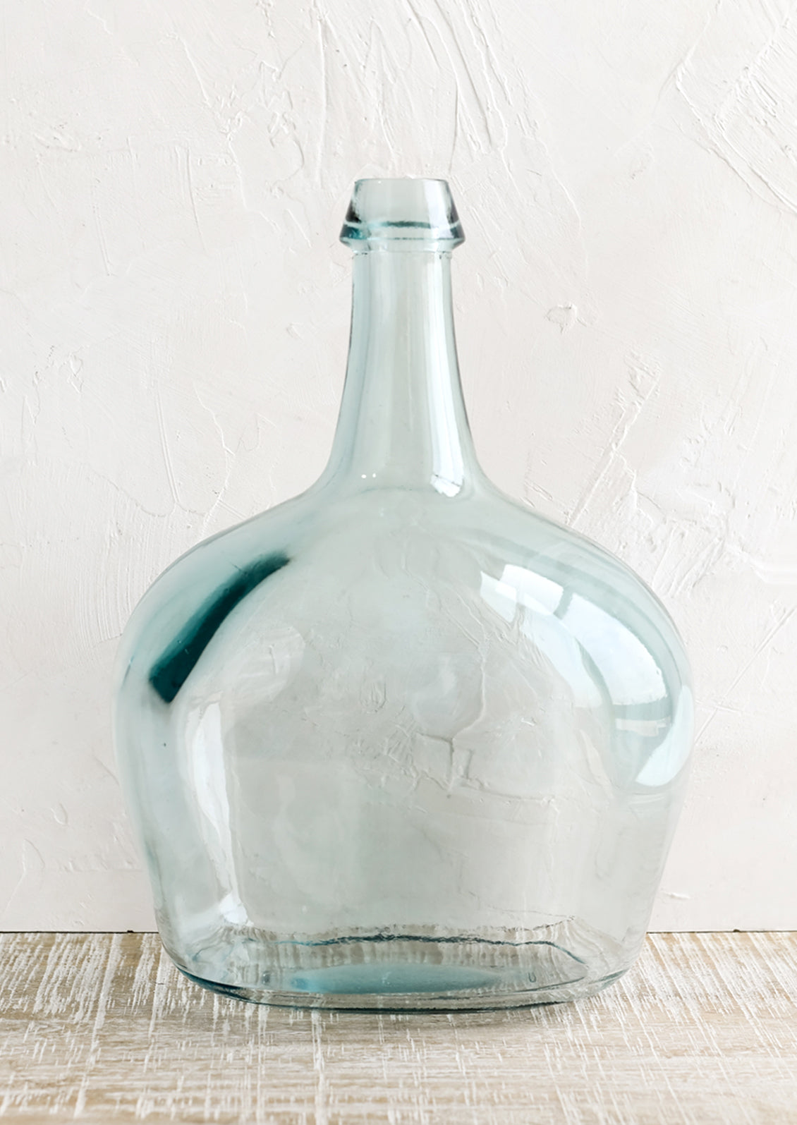 A large bottle shaped glass vase with blue tint.