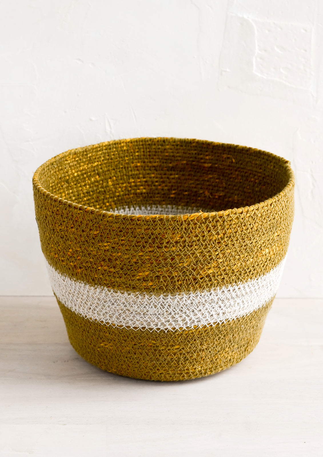 A round seagrass storage basket in ochre color with white stripe across middle.