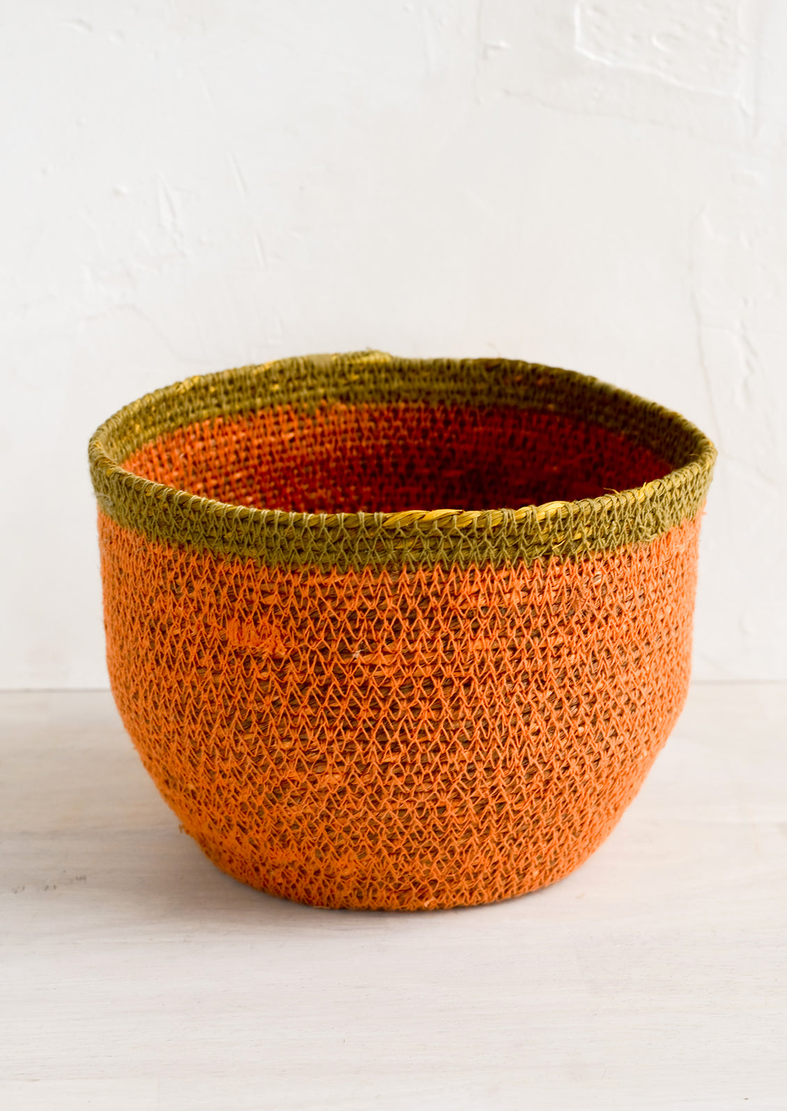 A round seagrass storage basket in coral color with ochre stripe around top.